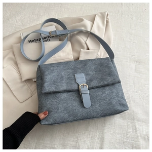 Détail d'un sac cabas gris-bleu mat avec lanière en cuir et boucle dorée sur un blazer