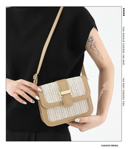 Close-up of woven straw shoulder bag with brown leather trim and golden H-clasp