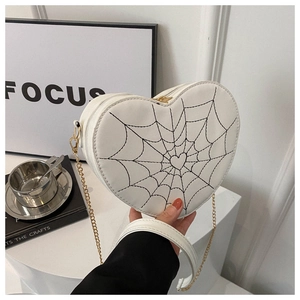 Detail of white heart-shaped bag featuring black spider web embroidery and gold chain