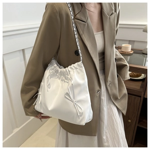 Detail of white drawstring tote bag with ribbon bow and metal chain strap on model