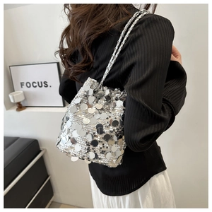 Close-up of silver sequin bucket bag with chain strap worn by a model in a minimalist setting