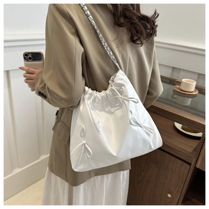 Detail of white tote bag featuring decorative bows and silver metal chain strap