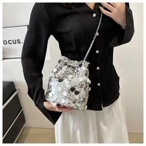 Silver sequin bucket bag with metal chain strap worn by a model in a modern studio