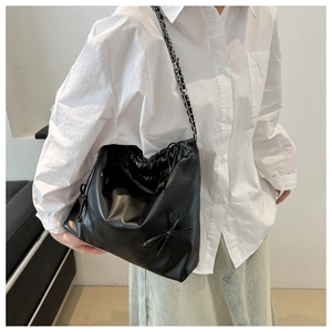 Detail of black drawstring tote bag featuring leather bow accents and metal chain strap