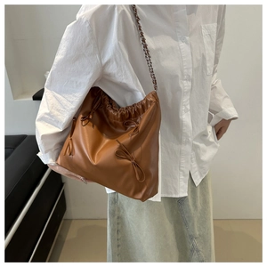 Brown leather shoulder bag with drawstring pleats and bow detail on a white background