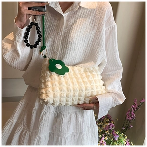 Detail of beige bubble texture shoulder bag with green flower charm and black beaded strap