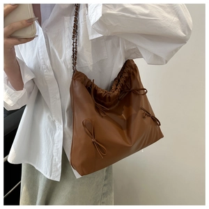 Detail of a brown leather tote bag featuring multiple 3D bows and a chain strap