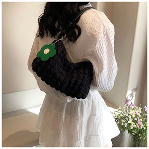 Detail of black bubble texture shoulder bag with green flower charm on a model