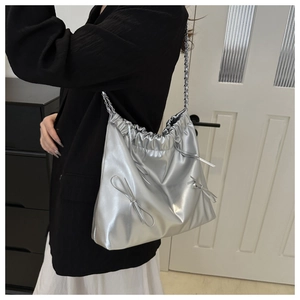 Detail of silver metallic tote bag with drawstring closure and bow accents on a model
