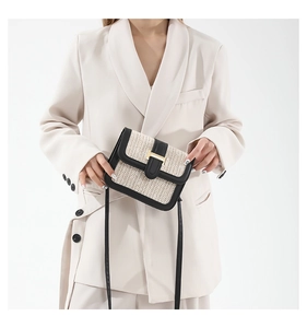 Close-up of woven straw crossbody bag with black leather trim and golden H-shaped clasp