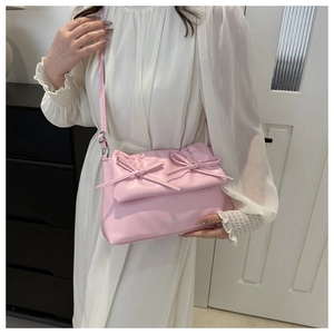 Détail d'un sac à bandoulière rose en cuir PU avec des nœuds sur une robe blanche