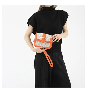 Detail of a woven cream shoulder bag with orange leather trim and golden metal clasp