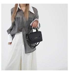 Détail du sac bandoulière noir mat avec logo doré et attaches métalliques dorées