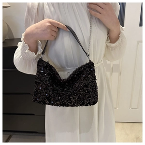 Detail einer funkelnden schwarzen Pailletten-Abendtasche mit Silberkette auf weißem Kleid