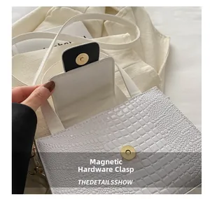 Gros plan sur le fermoir magnétique doré et la texture crocodile du sac à main blanc