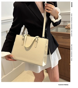Close-up of cream tote bag with adjustable shoulder strap and silver hardware on model