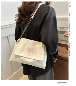 Detail of pink butterfly embroidery on a white crossbody bag with silver chain strap