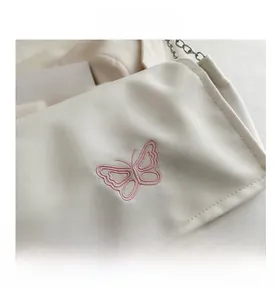 Détail de la broderie papillon rose et chaîne en métal argenté sur sac en tissu blanc