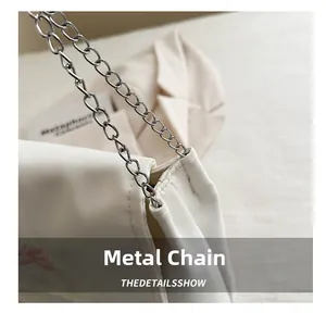 Détail de la chaîne en métal argenté et broderie rose sur le sac blanc en tissu
