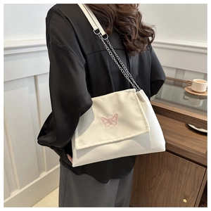 Détail de broderie papillon rose sur sac crème avec bandoulière élégante en chaîne métal