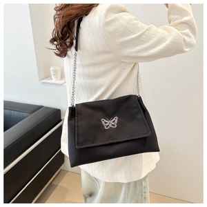 Détail d'un sac à bandoulière noir avec broderie papillon blanc et chaîne en argent