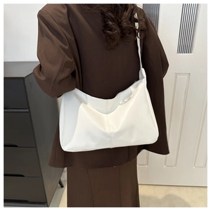 Dettaglio di una borsa hobo bianca minimalista indossata con un blazer marrone chic
