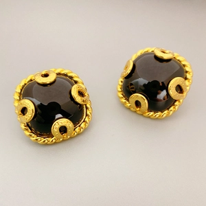 Macro detail of vintage gold-tone earrings with black gemstone and twist rope texture