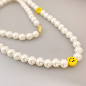 Elegant pearl necklace with two yellow smiley face beads and gold lobster clasp closure