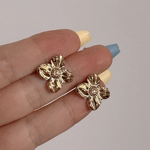 Golden flower earrings with four petals and textured finish shown on fingers for size