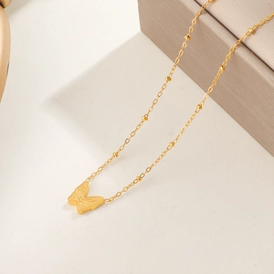 Collana con ciondolo a farfalla dorata minimalista con catena a sfere su sfondo beige