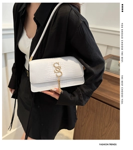 Close-up of white crocodile pattern shoulder bag with gold logo and tassel detail