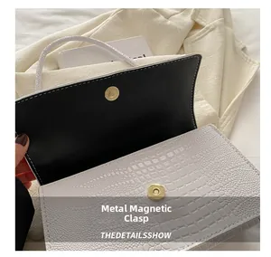 Detail of white crocodile-embossed bag featuring a round golden magnetic snap closure