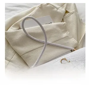 Close-up of white embossed leather handbag with gold logo detail and slim strap