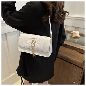 Detail of white crocodile embossed texture and golden tassel logo on crossbody bag