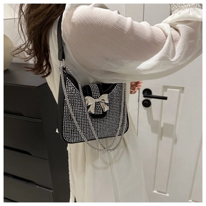 Détail d'un sac à bandoulière noir avec strass argentés et décoration de nœud en métal