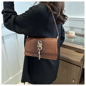 Detailed close-up of brown crocodile texture shoulder bag with gold S-buckle and tassel