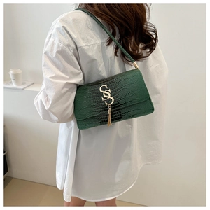Detail of dark green crocodile texture handbag with golden SS logo and tassel charm