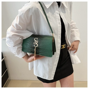 Detailed view of dark green crocodile texture bag with gold SS logo and tassel