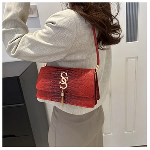 Detail of red croc-embossed leather handbag with gold SS logo and stylish tassels