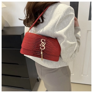 Detail of red croc-embossed shoulder bag featuring a gold S-clasp and chain tassel