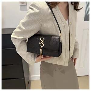 Detail of crocodile embossed leather texture with gold S logo and tassel on black shoulder bag