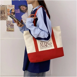 Detail of red and white canvas tote bag with ALONE print worn by a fashion model
