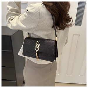 Close-up of black crocodile pattern shoulder bag with gold metal SS logo and fringe tassel