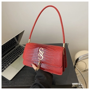 Detail of red crocodile texture handbag featuring golden S-logo and metal tassel charms
