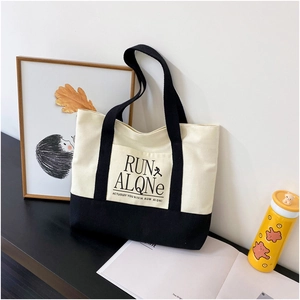 Detail shot of a contrast canvas tote bag with black trim and Run Alone print design