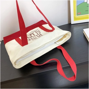 Detail of red and white canvas tote bag with contrast handles and top zipper closure