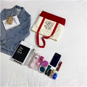 Flat lay of red and white canvas tote bag with Run Alone print and lifestyle items