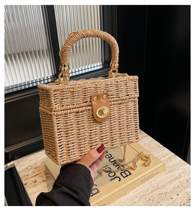 Close-up of hand-held woven straw bag with golden chain strap and leather buckle