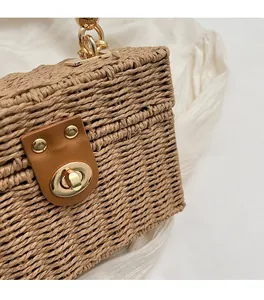 Close-up of woven straw handbag with brown leather clasp and gold twist lock detail