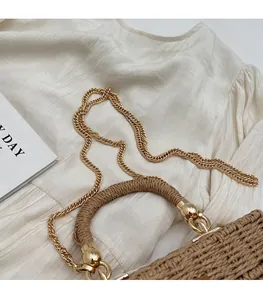 Detail of hand-woven straw bag featuring a brown braided handle and gold metal chain strap